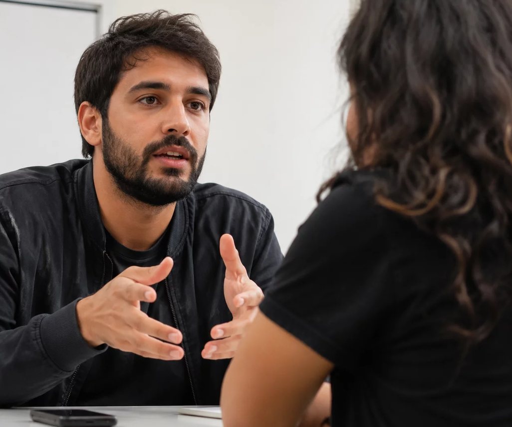 Uma pessoa sentada à mesa ergue a mão para pedir a palavra no meio da rodada